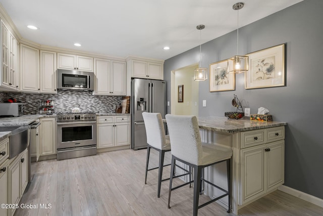 kitchen with appliances with stainless steel finishes, cream cabinetry, tasteful backsplash, a breakfast bar area, and light stone counters