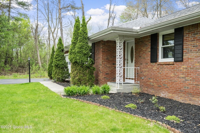 view of side of home with brick siding, a yard, and roof with shingles