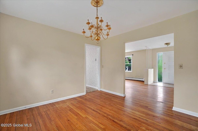 empty room with a chandelier, a baseboard radiator, light wood-style flooring, and baseboards
