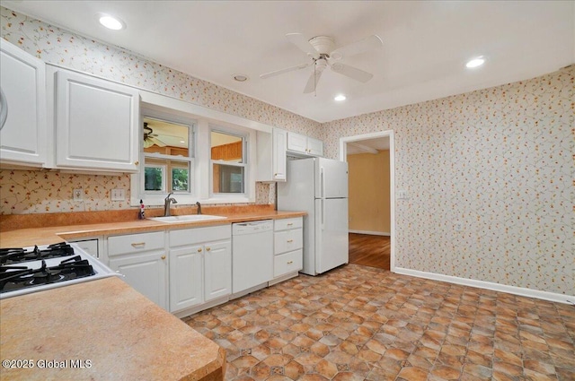 kitchen featuring white appliances, a sink, wallpapered walls, ceiling fan, and white cabinetry