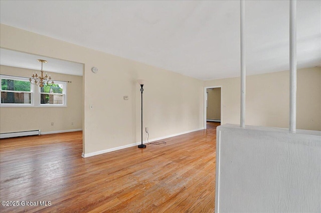 spare room featuring light wood-style flooring, baseboard heating, a chandelier, and baseboards
