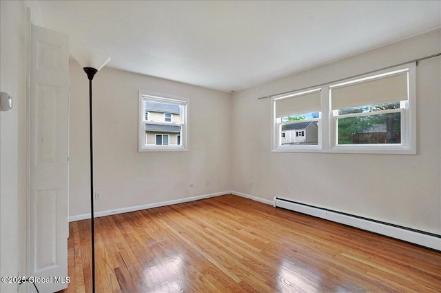 empty room with baseboard heating, light wood finished floors, and baseboards