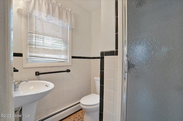 full bathroom with baseboard heating, a shower stall, toilet, tile walls, and a sink