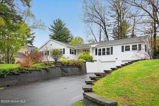 ranch-style home featuring stairway, an attached garage, asphalt driveway, and a front yard