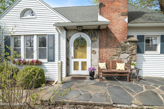 doorway to property with a shingled roof, a patio area, and a chimney