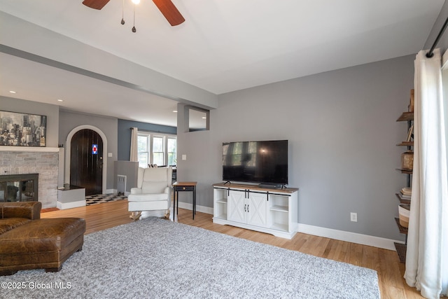 living area featuring a brick fireplace, a ceiling fan, baseboards, and light wood-style floors