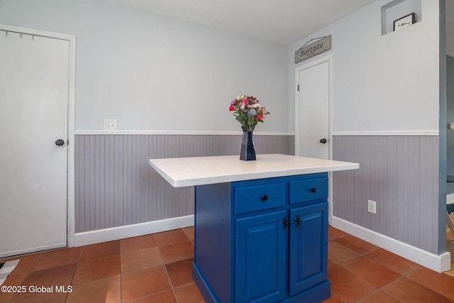 kitchen with dark tile patterned floors, blue cabinetry, a center island, wainscoting, and light countertops