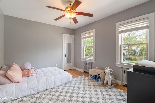 bedroom featuring radiator heating unit, baseboards, ceiling fan, and light wood-style flooring