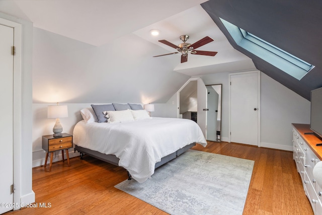 bedroom with a ceiling fan, baseboards, lofted ceiling with skylight, and light wood-type flooring