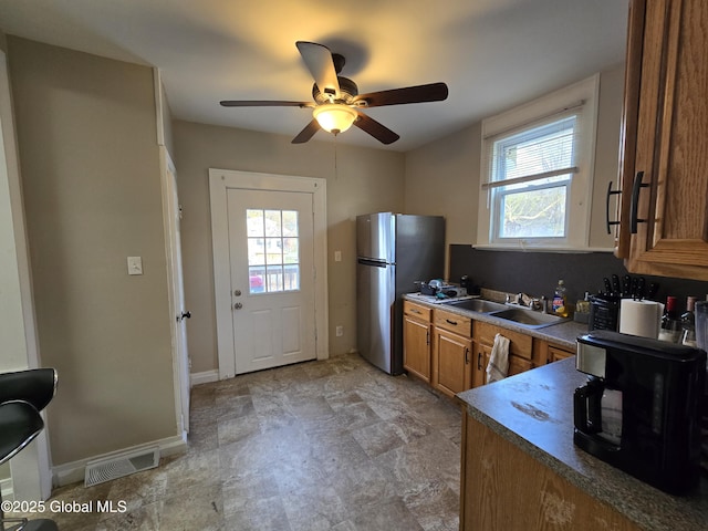 kitchen with ceiling fan, visible vents, brown cabinets, freestanding refrigerator, and a wealth of natural light
