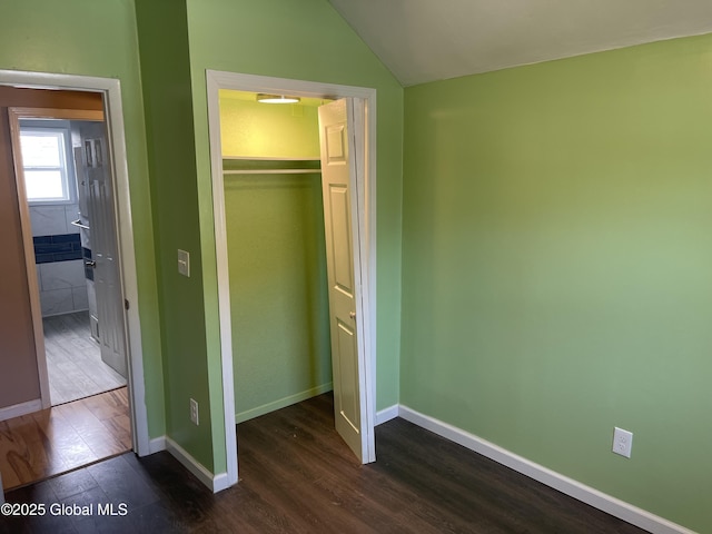unfurnished bedroom featuring dark wood-type flooring, baseboards, vaulted ceiling, and a closet