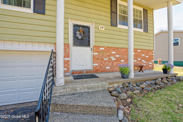 doorway to property with brick siding, an attached garage, and a porch