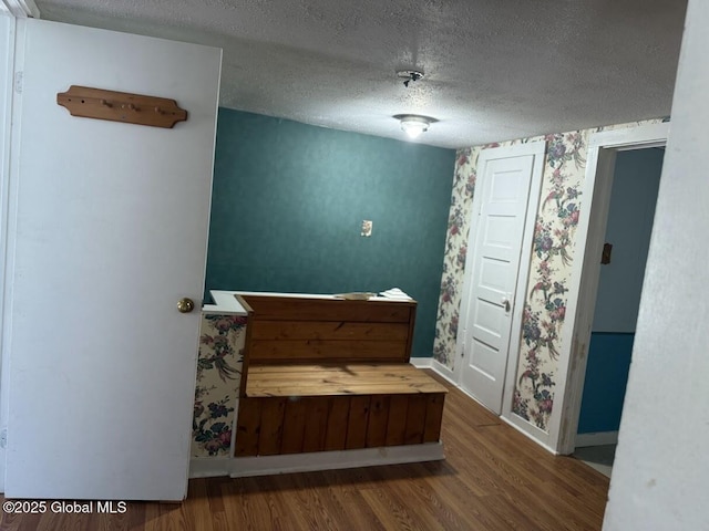 interior space with baseboards, a textured ceiling, wallpapered walls, and wood finished floors