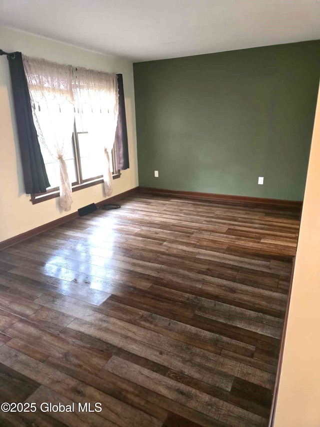 empty room featuring baseboards and dark wood-type flooring