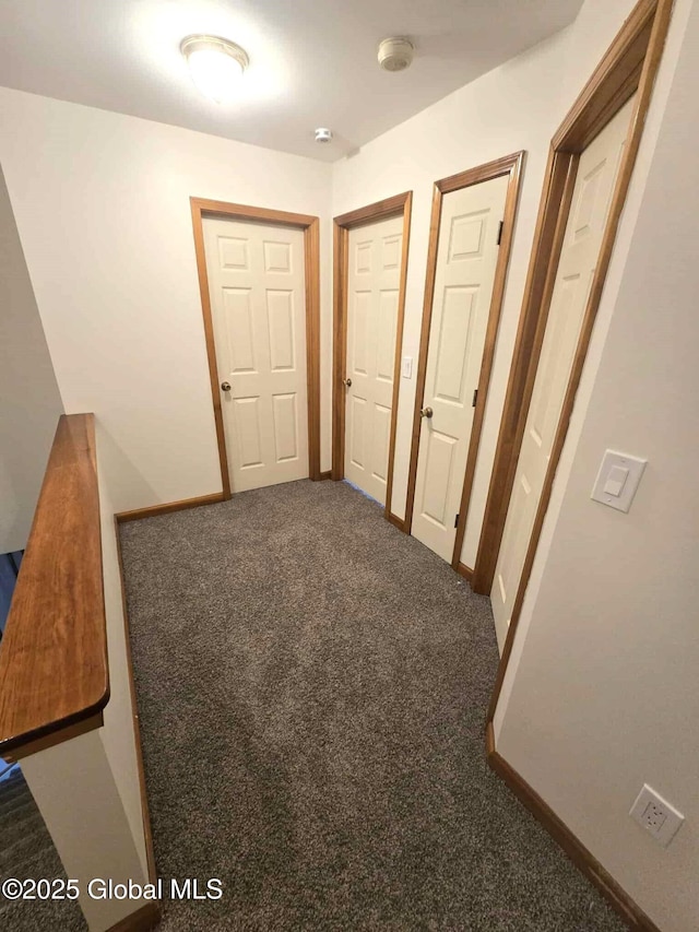 hall featuring dark colored carpet and baseboards