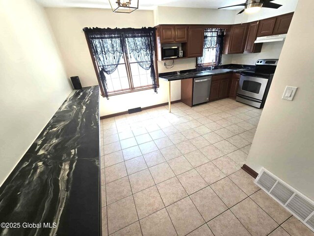 kitchen with light tile patterned flooring, dark countertops, under cabinet range hood, a ceiling fan, and appliances with stainless steel finishes