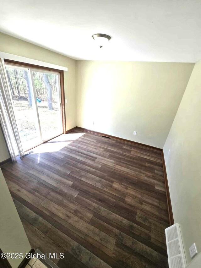 empty room featuring visible vents, dark wood-style flooring, and baseboards