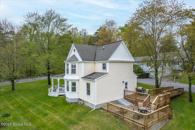 rear view of house featuring a lawn, roof with shingles, and a wooden deck