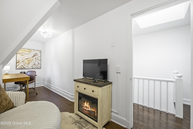 living area with baseboards, a glass covered fireplace, wood finished floors, and a skylight
