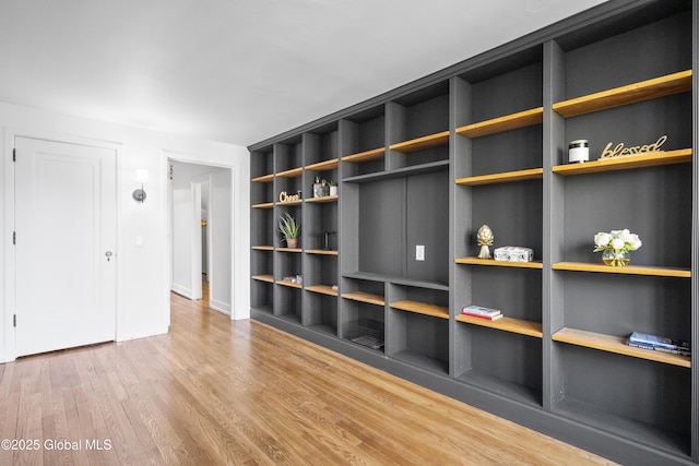 unfurnished living room featuring baseboards, built in features, and wood finished floors