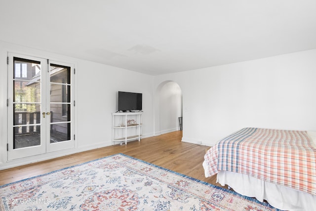 bedroom with access to outside, arched walkways, french doors, baseboards, and wood finished floors
