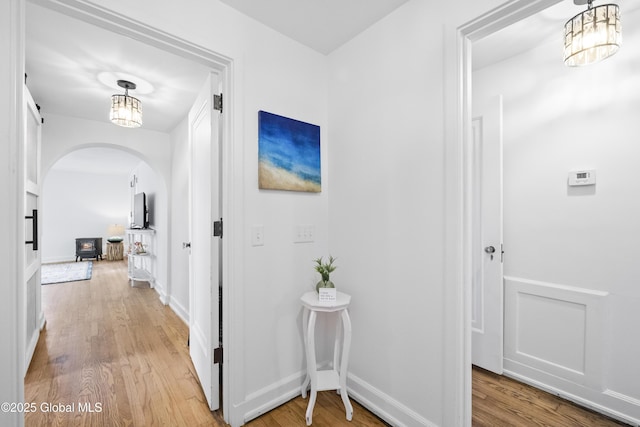 corridor with baseboards, arched walkways, and light wood-style flooring