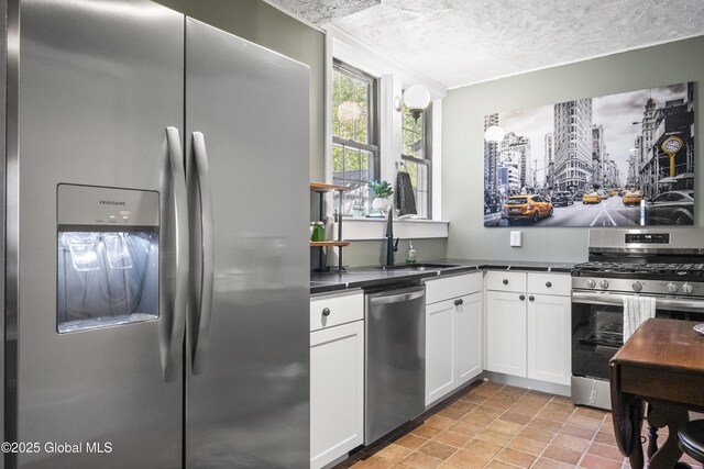 kitchen with dark countertops, a sink, a textured ceiling, stainless steel appliances, and white cabinetry