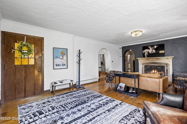living room featuring crown molding, arched walkways, a lit fireplace, and wood finished floors
