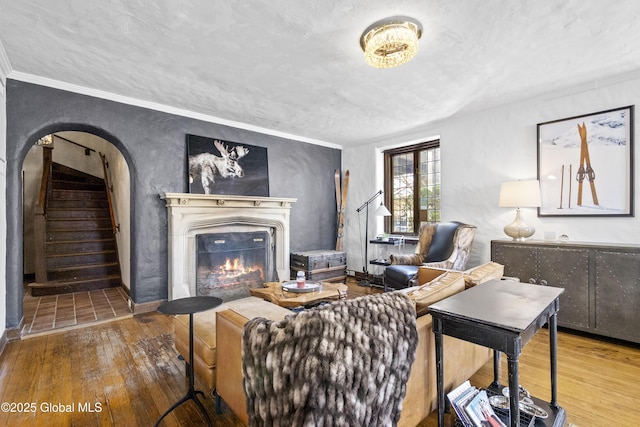 living area featuring stairway, arched walkways, hardwood / wood-style flooring, and a warm lit fireplace