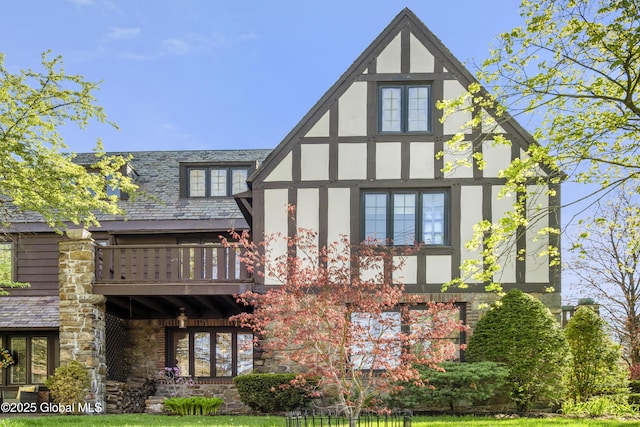 rear view of property with a high end roof, stucco siding, a balcony, and stone siding