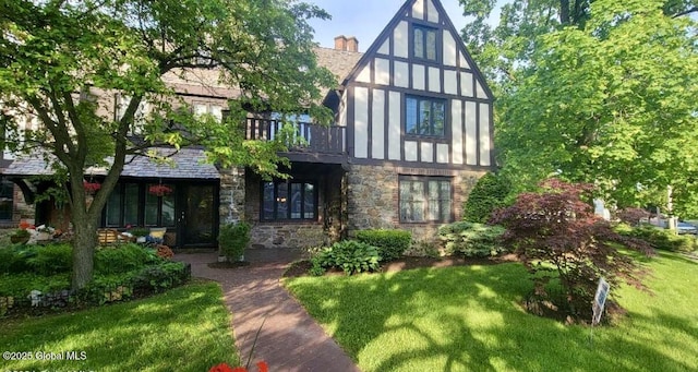 view of front of home with a chimney, a balcony, stone siding, and a front lawn