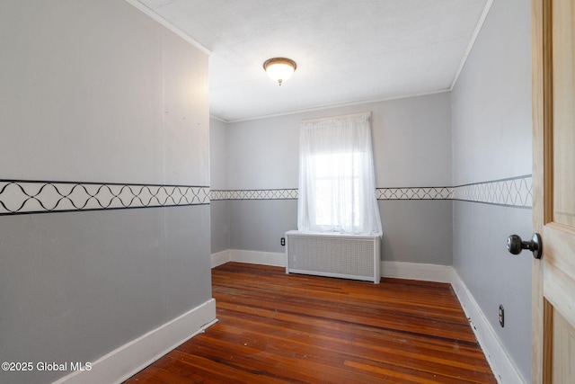 empty room featuring crown molding, radiator heating unit, baseboards, and wood-type flooring