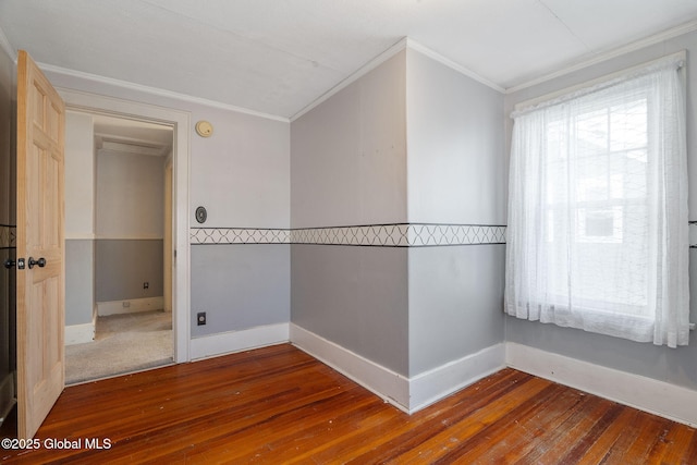empty room featuring wood-type flooring, baseboards, and ornamental molding