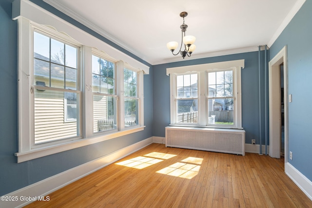 unfurnished dining area featuring an inviting chandelier, ornamental molding, wood-type flooring, baseboards, and radiator heating unit
