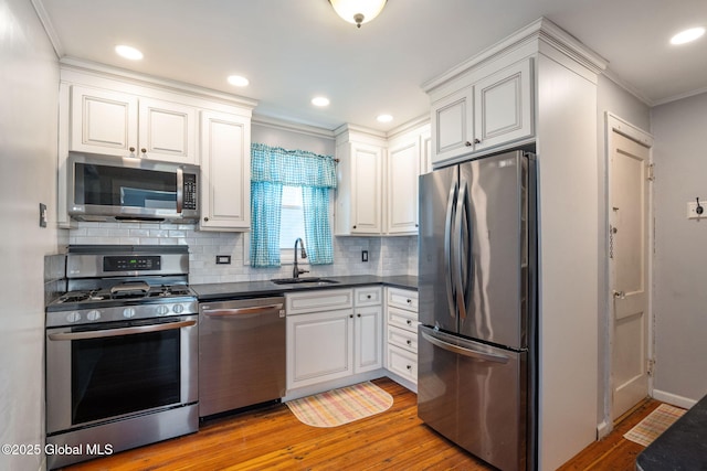 kitchen with appliances with stainless steel finishes, dark countertops, a sink, light wood finished floors, and ornamental molding