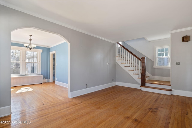 unfurnished living room featuring arched walkways, light wood finished floors, radiator heating unit, and a chandelier