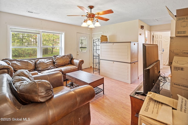 living room with light wood-style floors, visible vents, ceiling fan, and a textured ceiling
