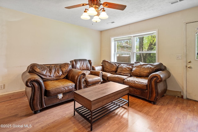 living area with light wood finished floors, a textured ceiling, a ceiling fan, and visible vents