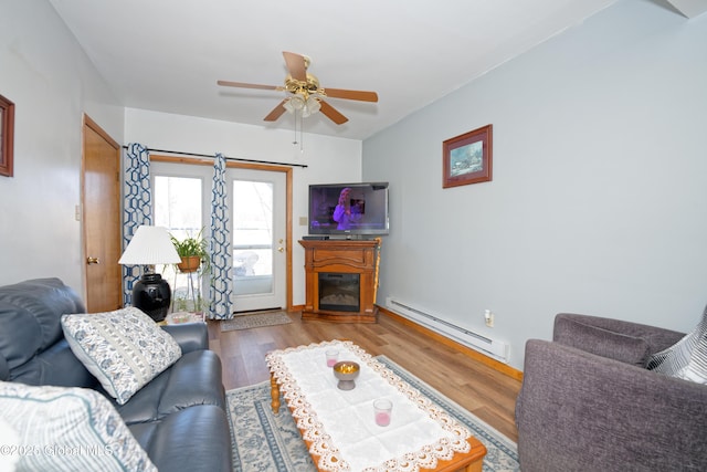 living room featuring a glass covered fireplace, baseboard heating, a ceiling fan, and wood finished floors