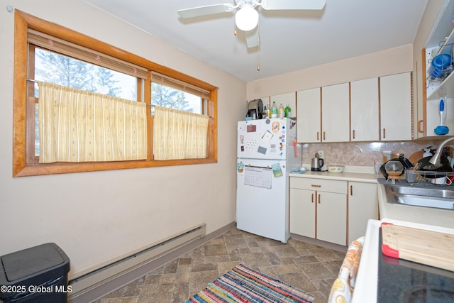 kitchen featuring freestanding refrigerator, stove, light countertops, a baseboard radiator, and stone finish flooring