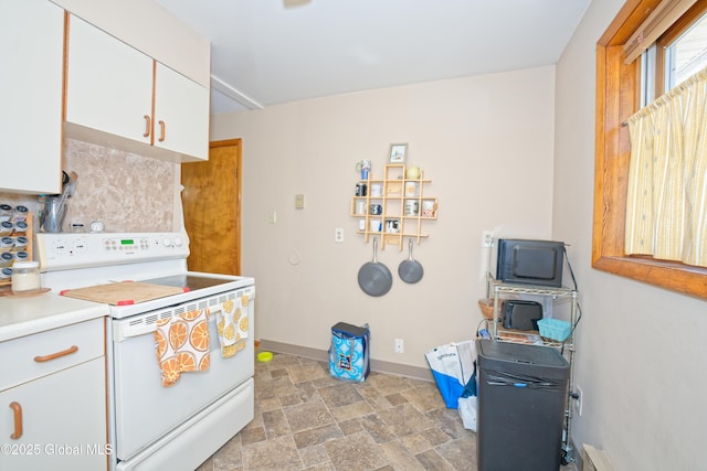 kitchen featuring baseboards, stone finish floor, light countertops, white cabinets, and electric stove