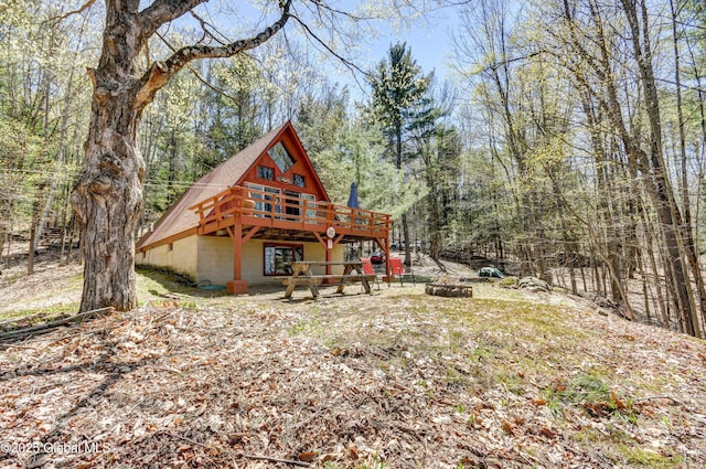 back of property featuring a wooded view, a fire pit, and a wooden deck