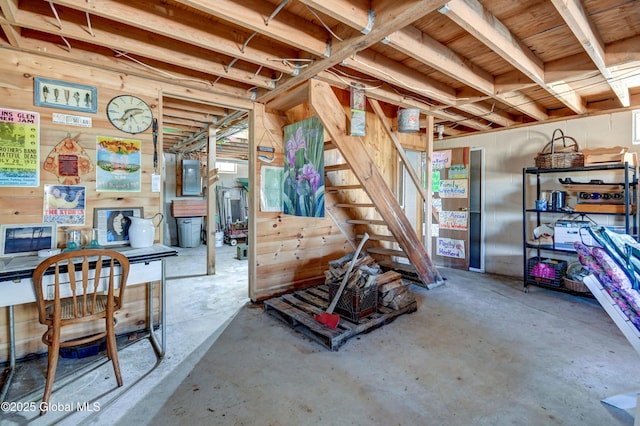 basement with electric panel, wooden walls, and stairway