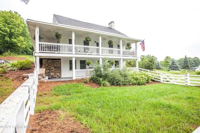 rear view of house with fence, a balcony, stone siding, a chimney, and a yard