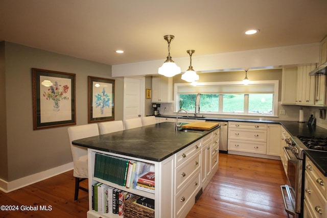 kitchen featuring dark countertops, dark wood finished floors, stainless steel appliances, white cabinetry, and a kitchen bar