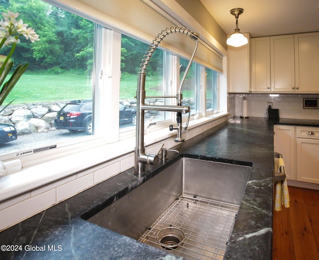 kitchen with hanging light fixtures, tasteful backsplash, wood finished floors, a sink, and dark stone counters
