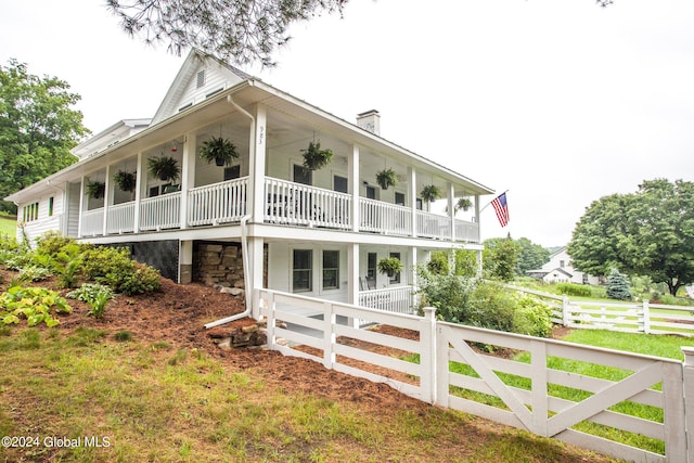 rear view of house featuring covered porch, a fenced front yard, a chimney, and a balcony