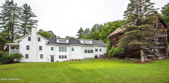 rear view of property with a shingled roof, a yard, and a chimney