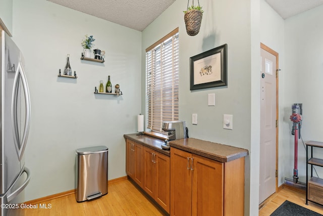 bar with light wood-style floors, freestanding refrigerator, a textured ceiling, and baseboards