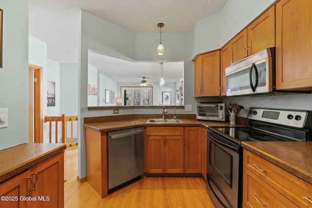 kitchen with stainless steel appliances, brown cabinetry, a sink, and light wood-type flooring